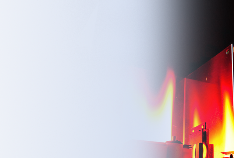 Eine Laborumgebung mit einem brennenden Elementanalysator im Hintergrund. Der Analysator hat eine rechteckige Form und ist aus Metall.