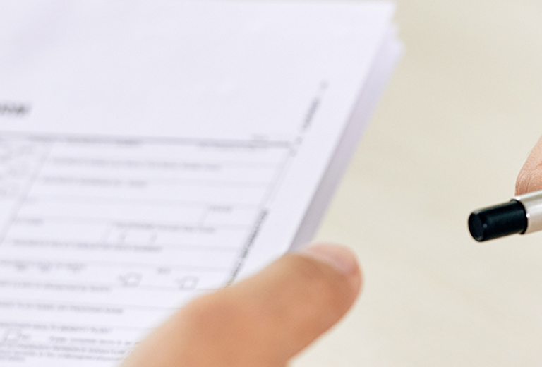 Eine Hand reicht einen Stift an eine andere Hand, während ein Kontaktformular auf einem Tisch liegt.