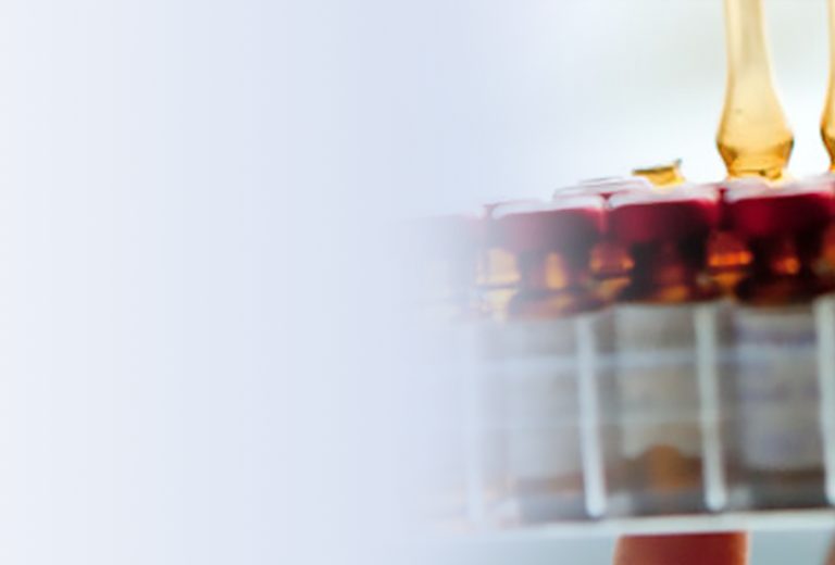 Reihe von Ampullen mit orangefarbenem Inhalt und roten Kappen, gehalten von einer Hand. 