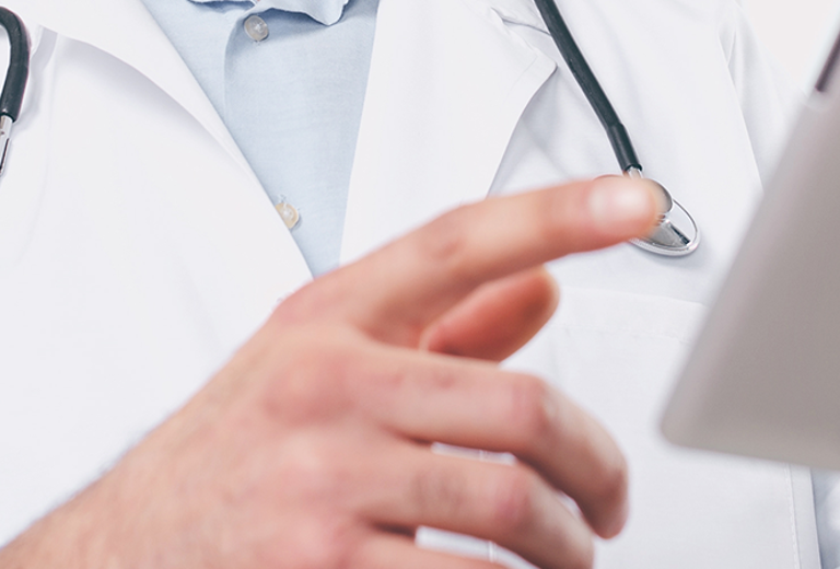 Ein Arzt mit Stethoskop hält ein Tablet in der Hand und zeigt darauf. Der Arzt trägt einen weißen Kittel.