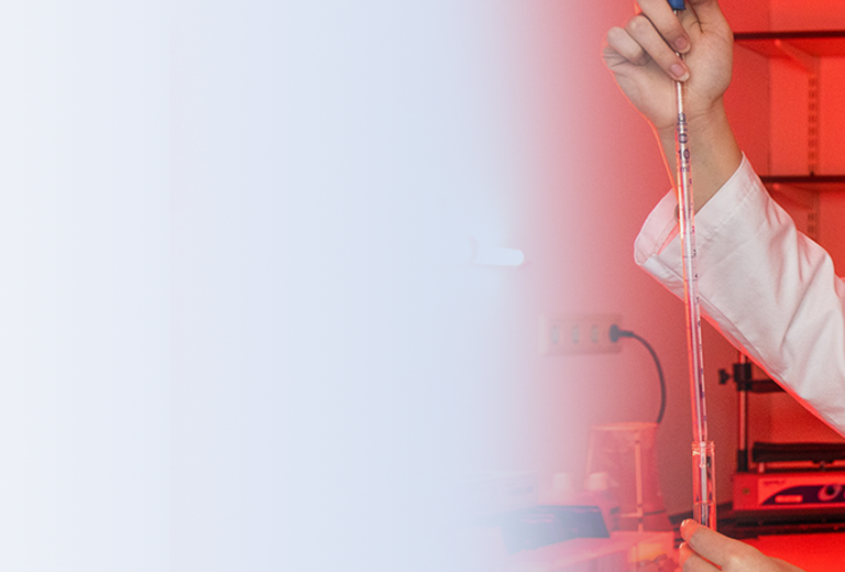 Eine Laborantin in einem weißen Laborkittel hält eine Pipette in der Hand und führt einen Test in einem roten beleuchteten Labor durch.