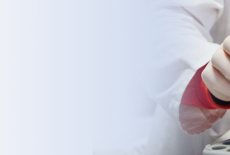 Eine Hand in einem weißen Laborkittel greift nach einem Reagenzglas mit buntem Verschluss in einem Labor mit mehreren Probenröhrchen.