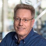 Dipl.-Inform. Thomas Kröger, sitzend, trägt ein blaues Hemd mit Karomuster. Im Hintergrund unscharfe Büroeinrichtung.