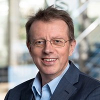  Der Arzt Dr. Andreas Gerritzen trägt einen dunklen Anzug und hellblaues Hemd, steht vor unscharfem Hintergrund