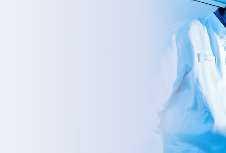 Eine Person in einem weißen Laborkittel arbeitet an einem wissenschaftlichen Gerät in einem Labor. Der Hintergrund zeigt verschiedene Laborausrüstungen.