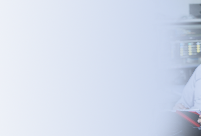 Zwei Personen sitzen an einem Schreibtisch mit Computerbildschirmen im Hintergrund.