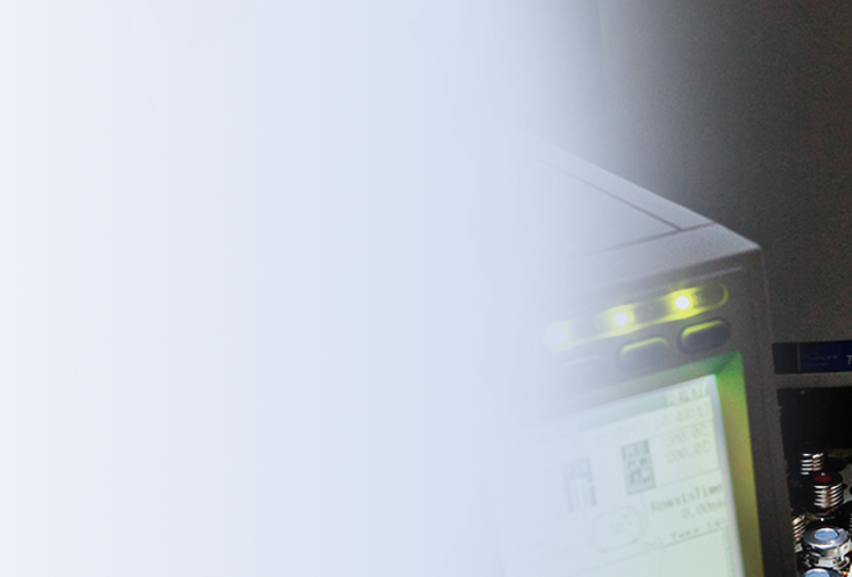 Eine Hand in einem weißen Handschuh hält ein Reagenzglas mit roter Flüssigkeit. Im Hintergrund sind Laborausrüstung und ein Bildschirm sichtbar.