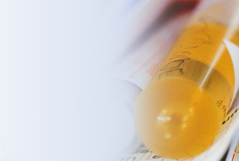 Nahaufnahme von mehreren Reagenzgläsern mit orangefarbenem Inhalt und Dokumenten, die teilweise übereinander liegen.