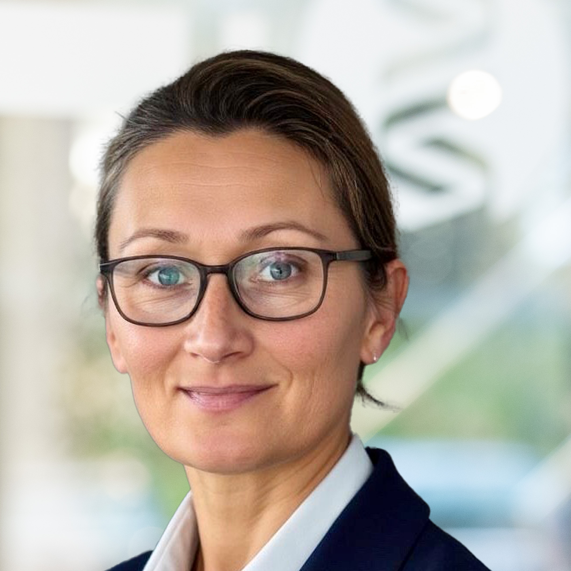 Anna Kuhlenkamp, Senior-Personalreferentin, trägt einen blauen Blazer und ein weißes Hemd. Sie steht in einem modernen Büro.