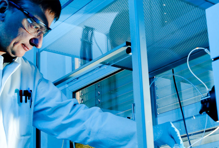 Forscher in weißem Laborkittel arbeitet an einem Analysegerät in einem Labor