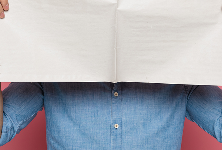 Eine Person in einem blauen Hemd hält eine große Zeitung vor dem Gesicht. 
