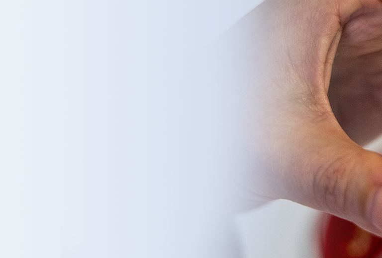 Eine Hand hält eine Petrischale mit blauen und roten Bakterienkulturen, die in einer spiralförmigen Anordnung wachsen.