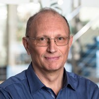 Der Arzt Dr. Andreas Sputtek trägt ein blaues Hemd und steht vor einem unscharfen Hintergrund