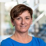 Birgit Arasmus, mit kurzem braunem Haar, trägt ein blaues Oberteil, steht in einem modernen Laborumfeld.